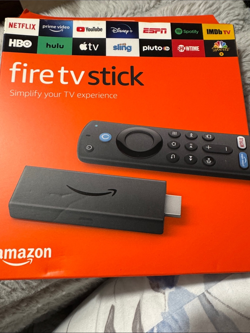 Amazon Fire TV Stick with Black Remote on Orange Packaging